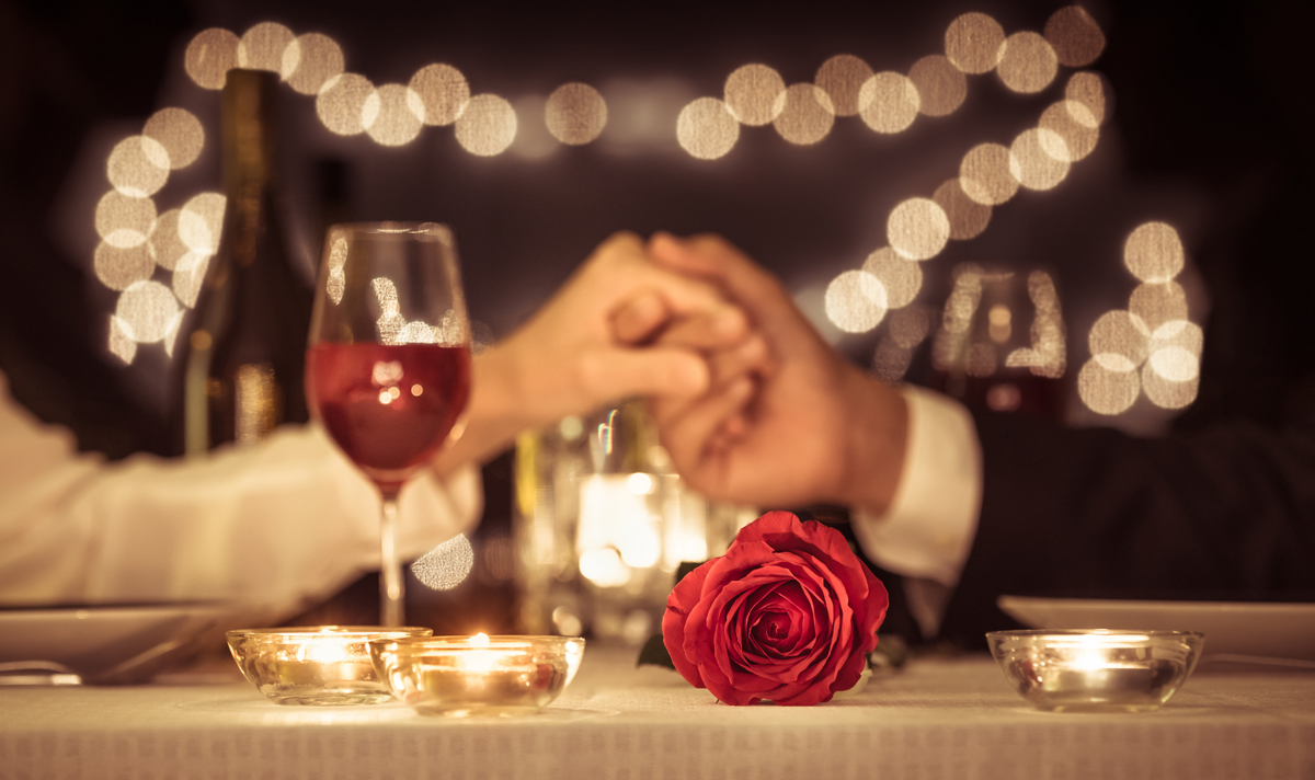 mani che si stringono a cena con calice e rosa atmosfera romantica luce calda